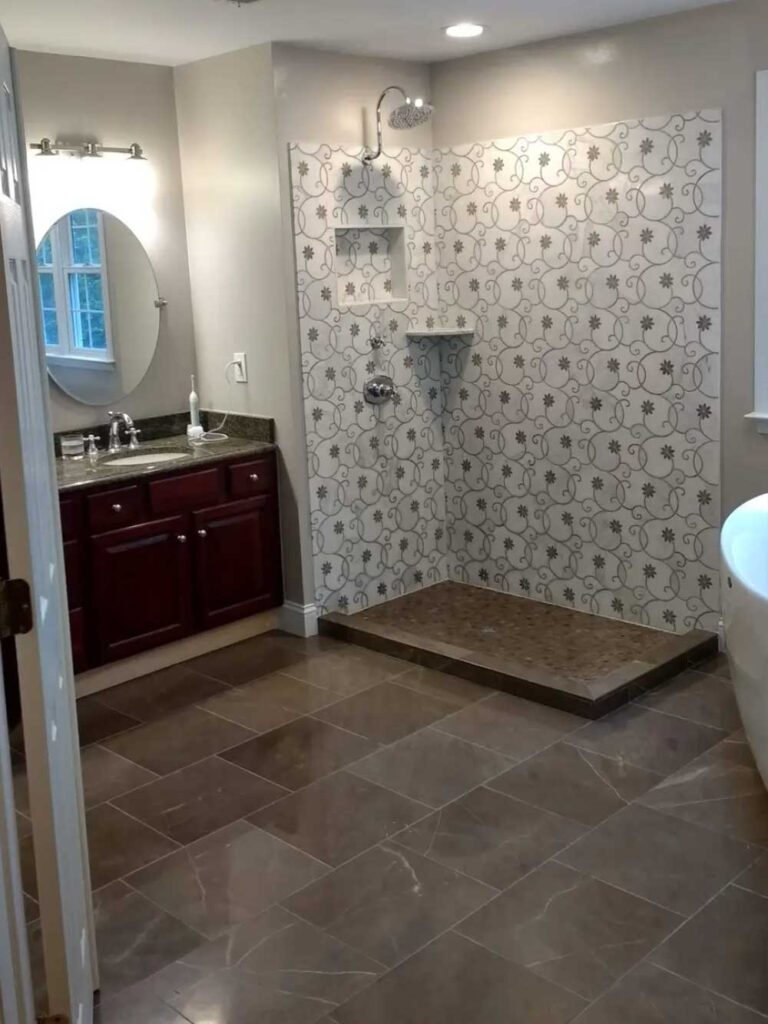 Tiled shower walls and base and tiled bathroom floor. Tiles niches and a stone shelf. Brown wood vanity with granite countertops.